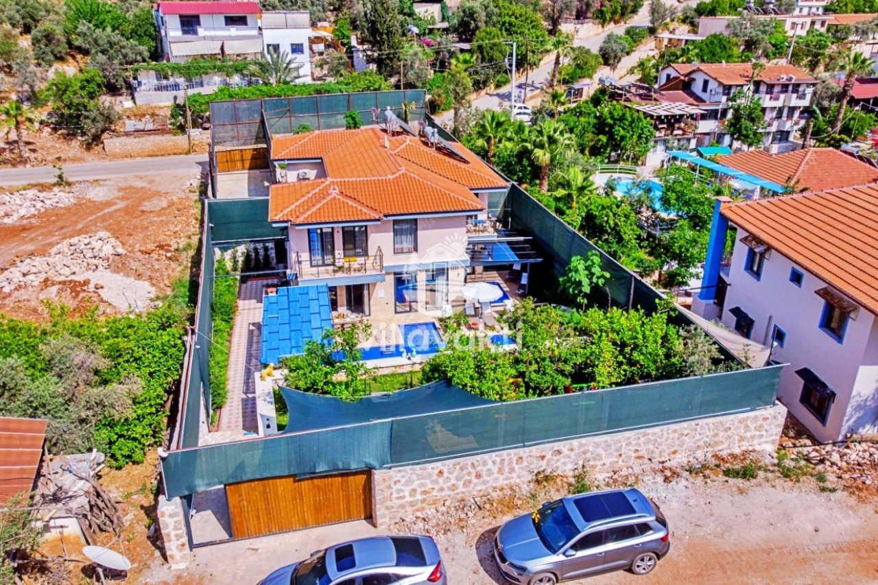 Ağaçlarla çevrili bahçesi ve havuzu olan iki katlı villanın havadan görünümü.