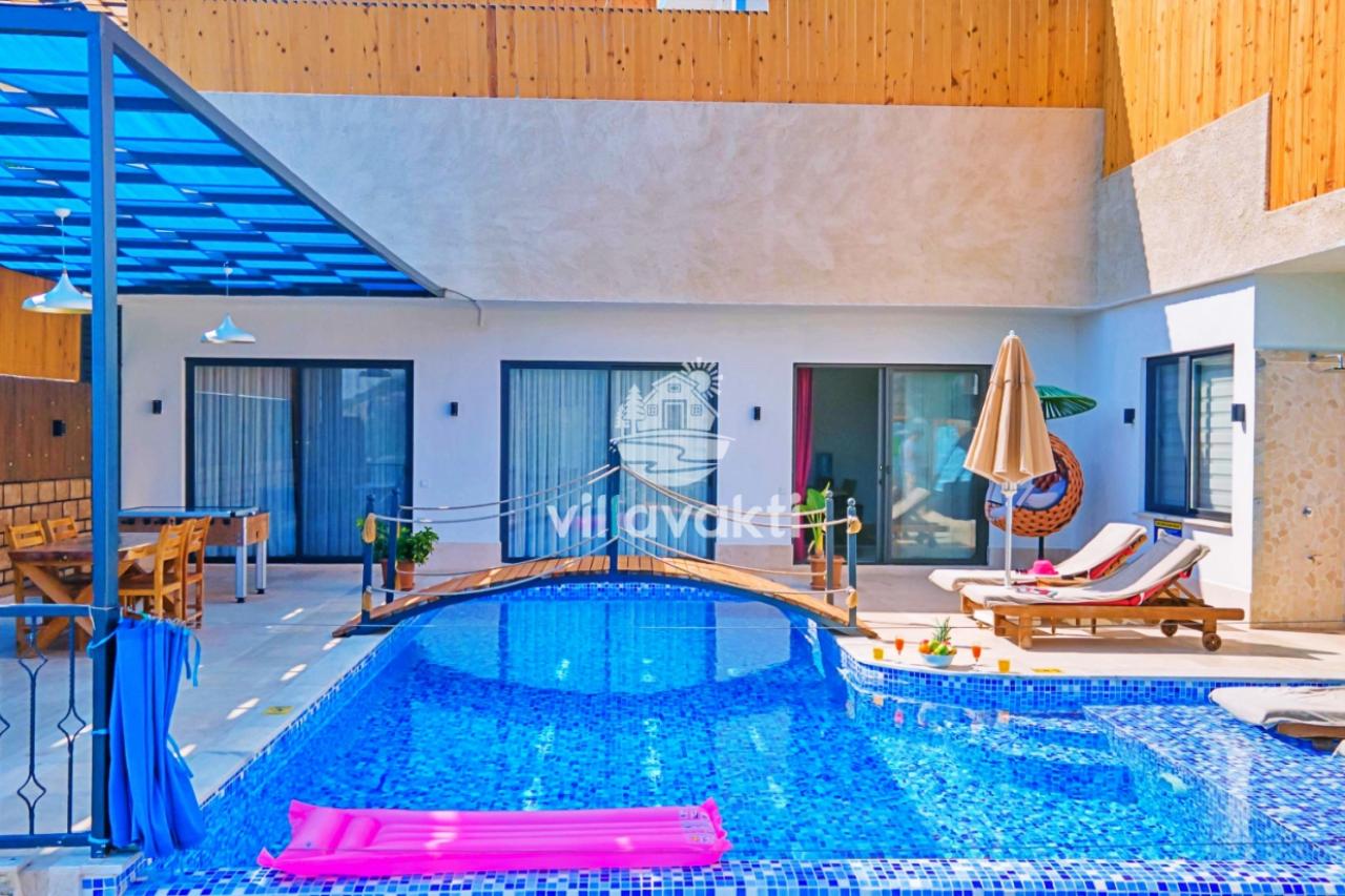 Mavi havuz üzerinde köprü bulunan, şezlong ve oturma alanlı modern villa bahçesi.