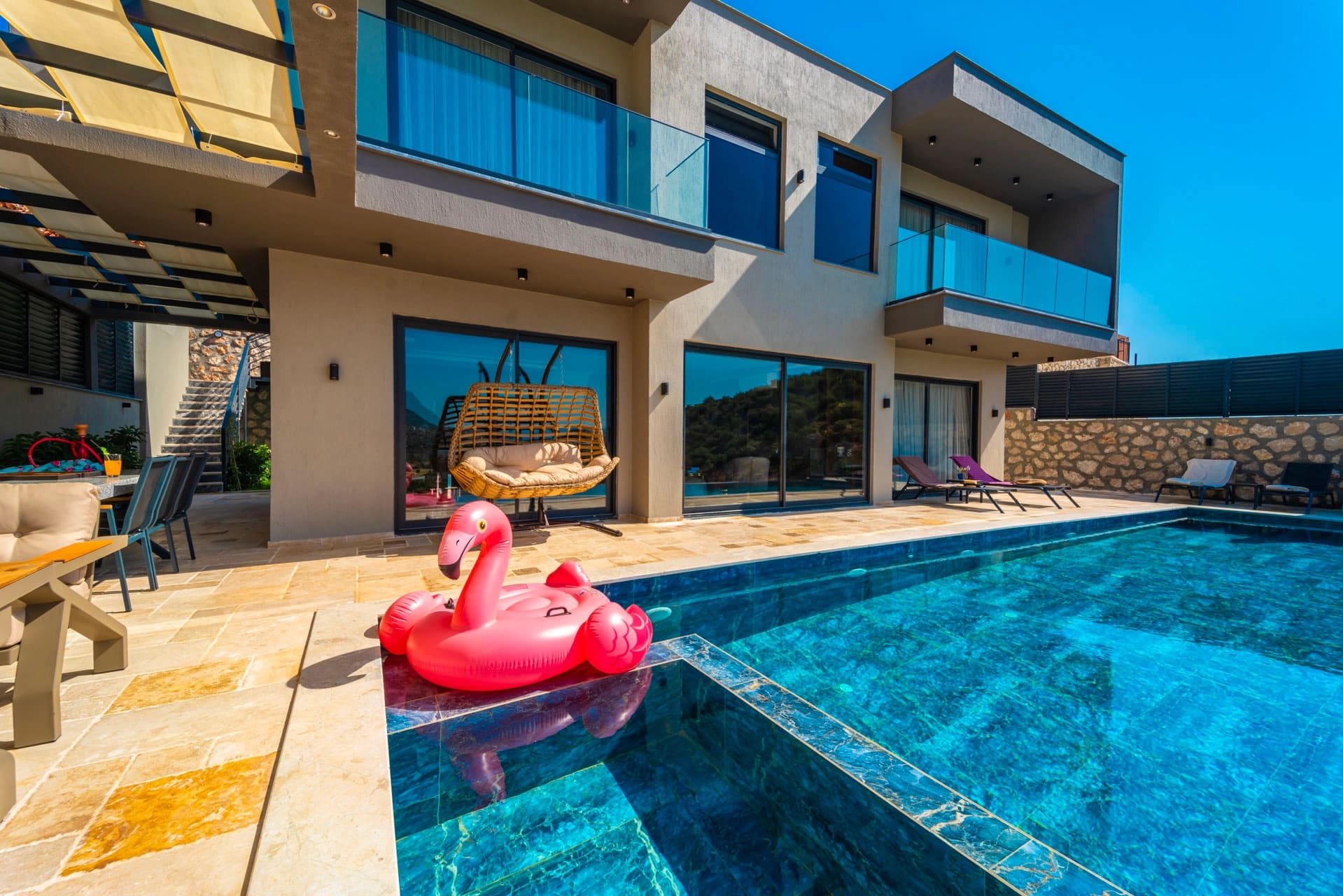 Güneşli havuz başında şezlonglar ve pembe flamingo simit olan modern villa.