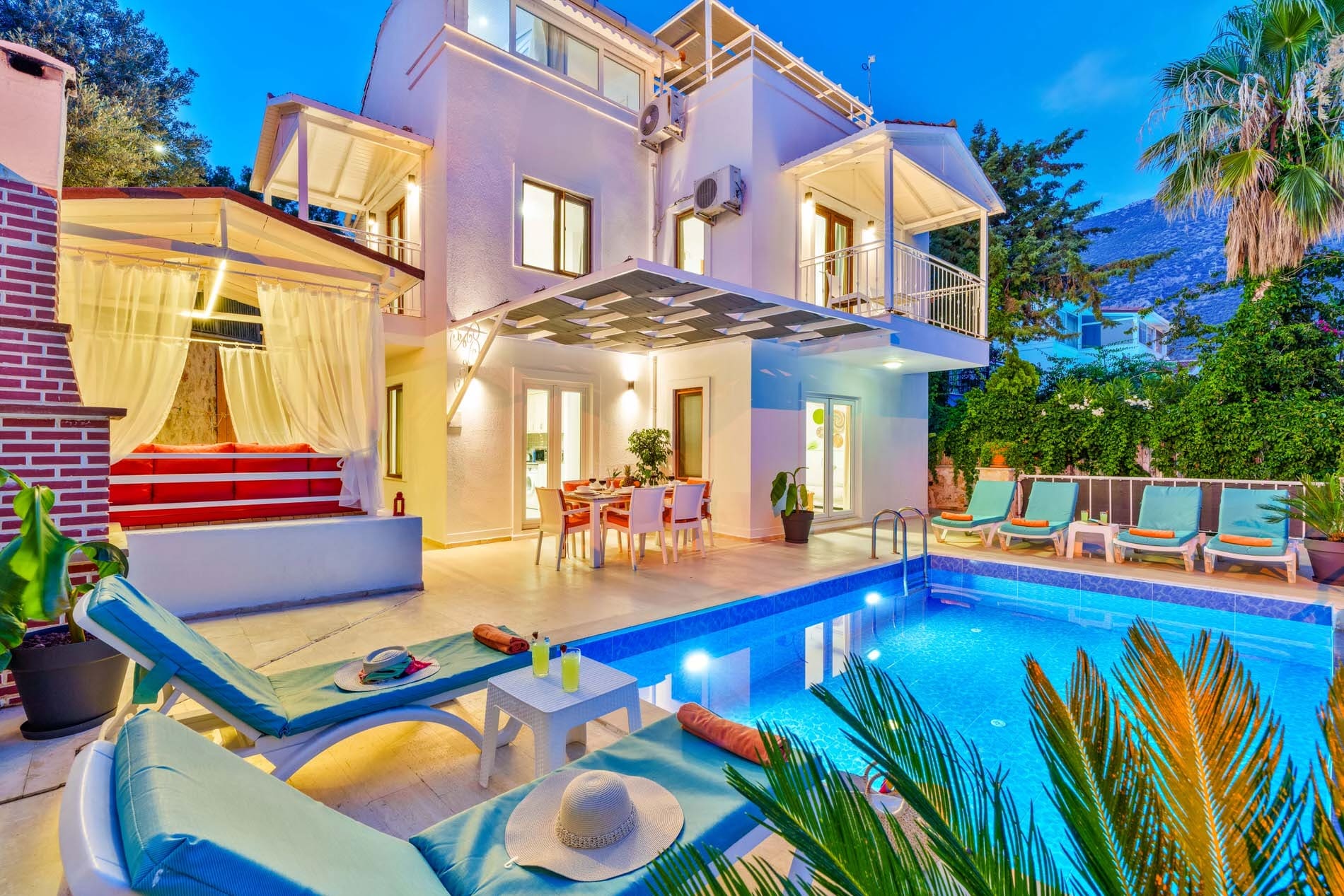 Akşam aydınlatmalı havuz kenarında şezlonglar ve iki katlı beyaz villa.
