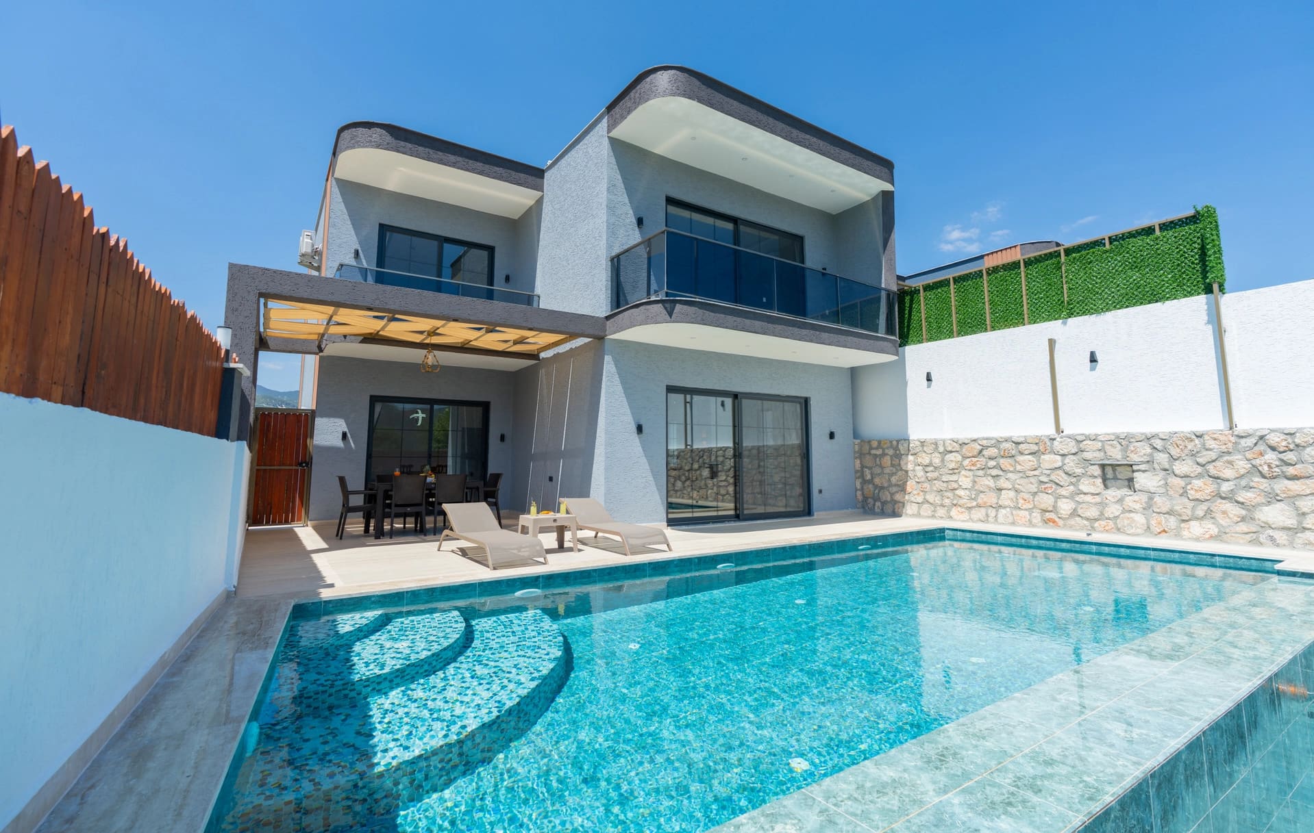 İki katlı modern gri villanın önünde havuz ve şezlonglar yer alıyor.