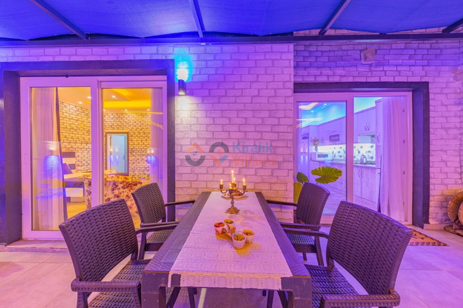 Akşam aydınlatmalı tuğla duvarlı terasta yemek masası ve sandalyeler.