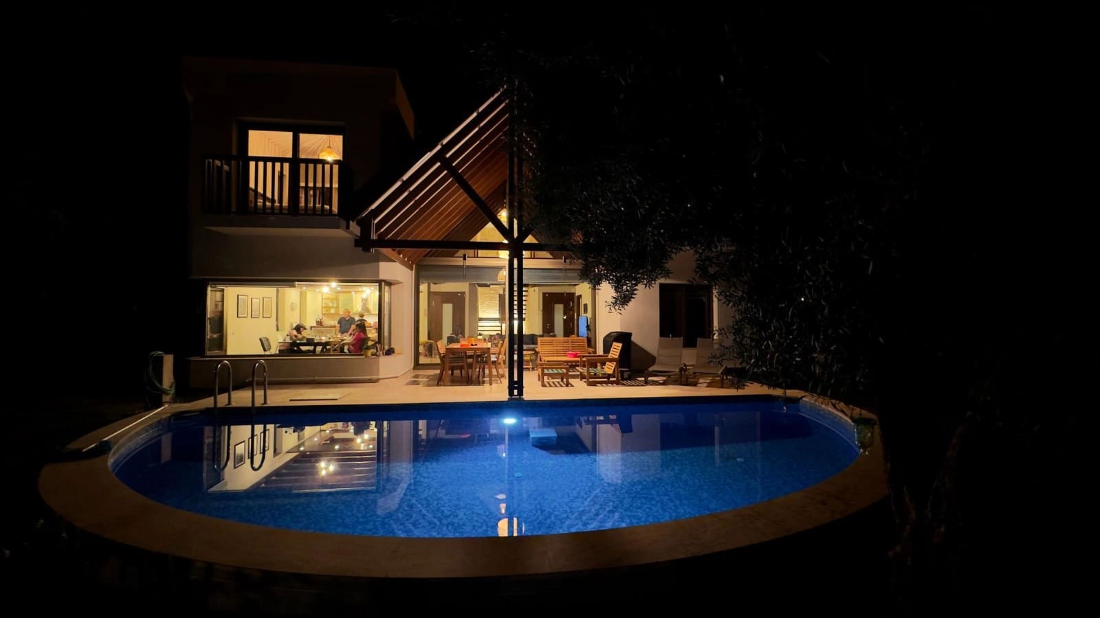 Gece aydınlatmalı havuz ve arka planda ışıkları yanan villa.
