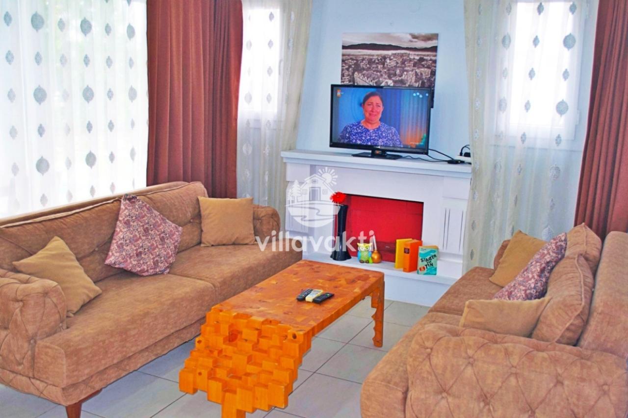 Kahverengi koltuklar, orta sehpa ve televizyon bulunan oturma odası.