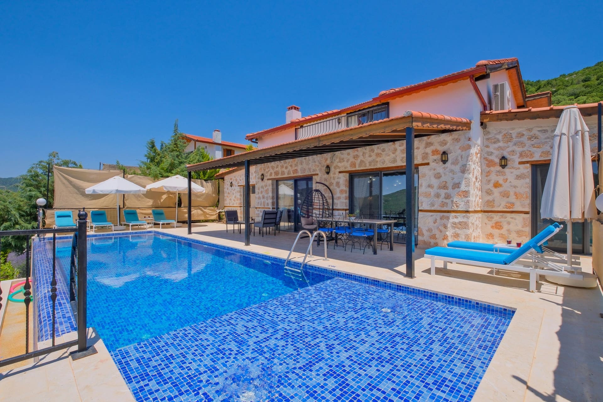 Mavi şezlongların bulunduğu havuz kenarı ve arkasında villa dış cephesi.