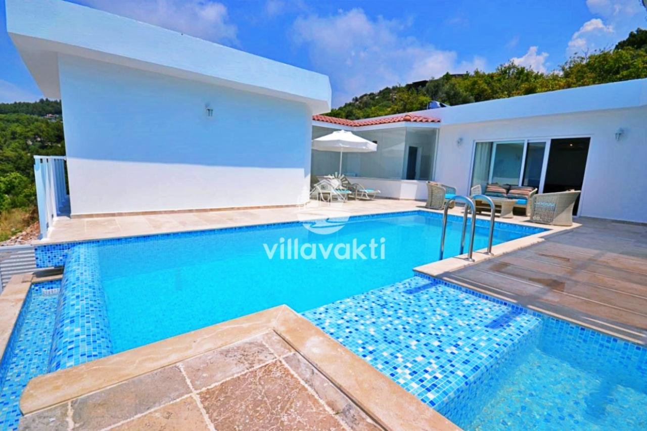 Açık renk taş terasta yer alan yüzme havuzu ve arka planda villa dış cephesi.