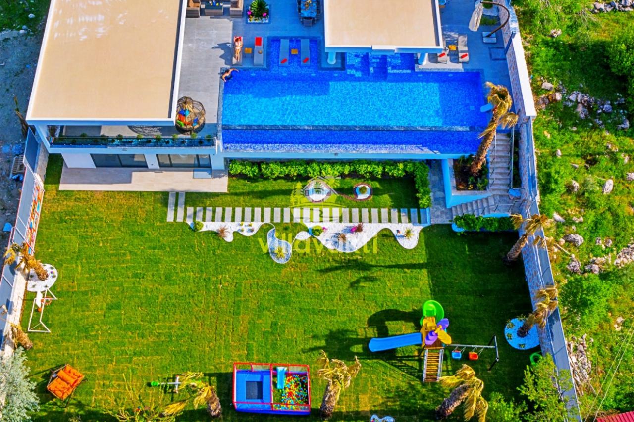 Büyük havuzlu ve bahçesinde oyun parkı bulunan villanın havadan görünümü.