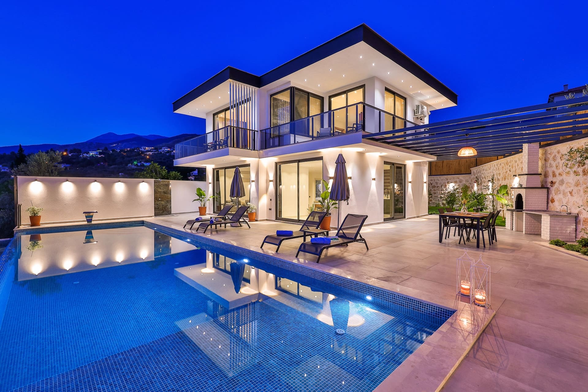 Işıklandırılmış modern dış cephesi, havuzu ve bahçe oturma grubuyla iki katlı villa.