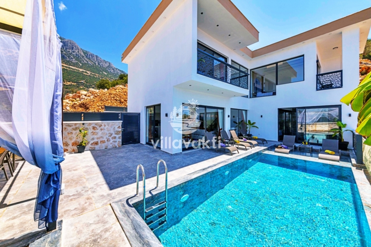Dağ manzaralı havuz kenarında şezlonglar ve iki katlı beyaz villa.