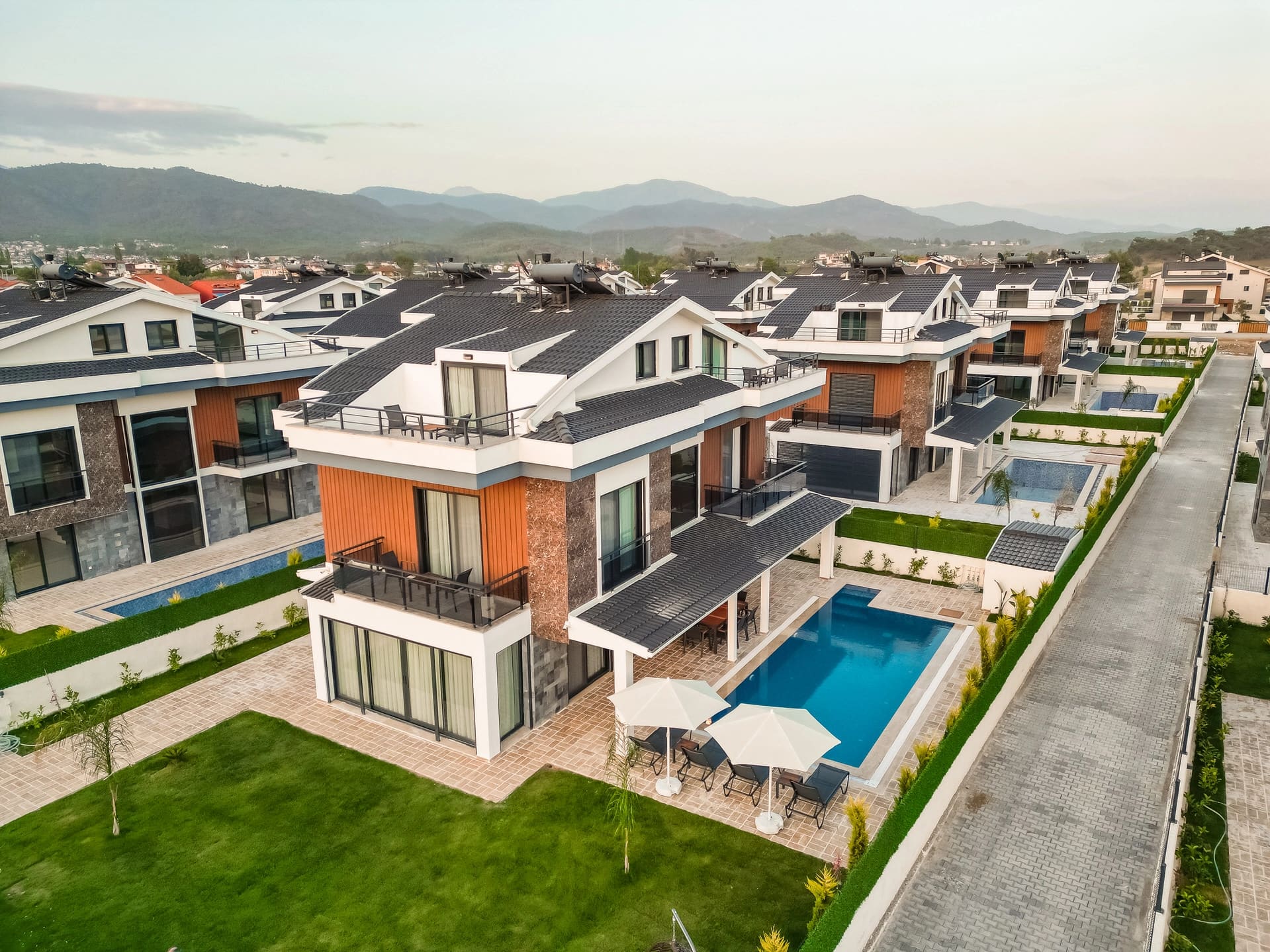 Havuzlu modern villaların yer aldığı site görünümü ve uzakta dağlar.