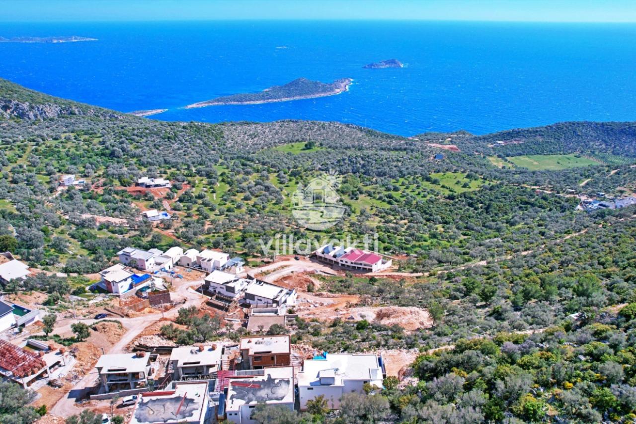 Ağaçlık alanın ortasında yer alan villalara ve uzaktaki denize bakan yüksek açı manzarası.