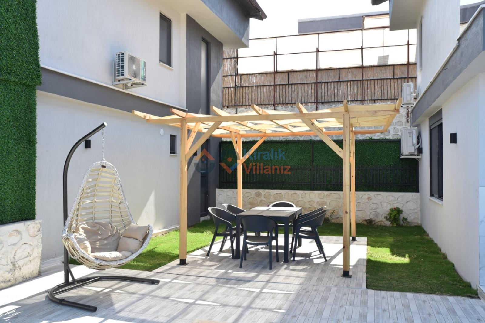 Bahçede ahşap pergolalı oturma grubu ve salıncak bulunan villa dış alanı.
