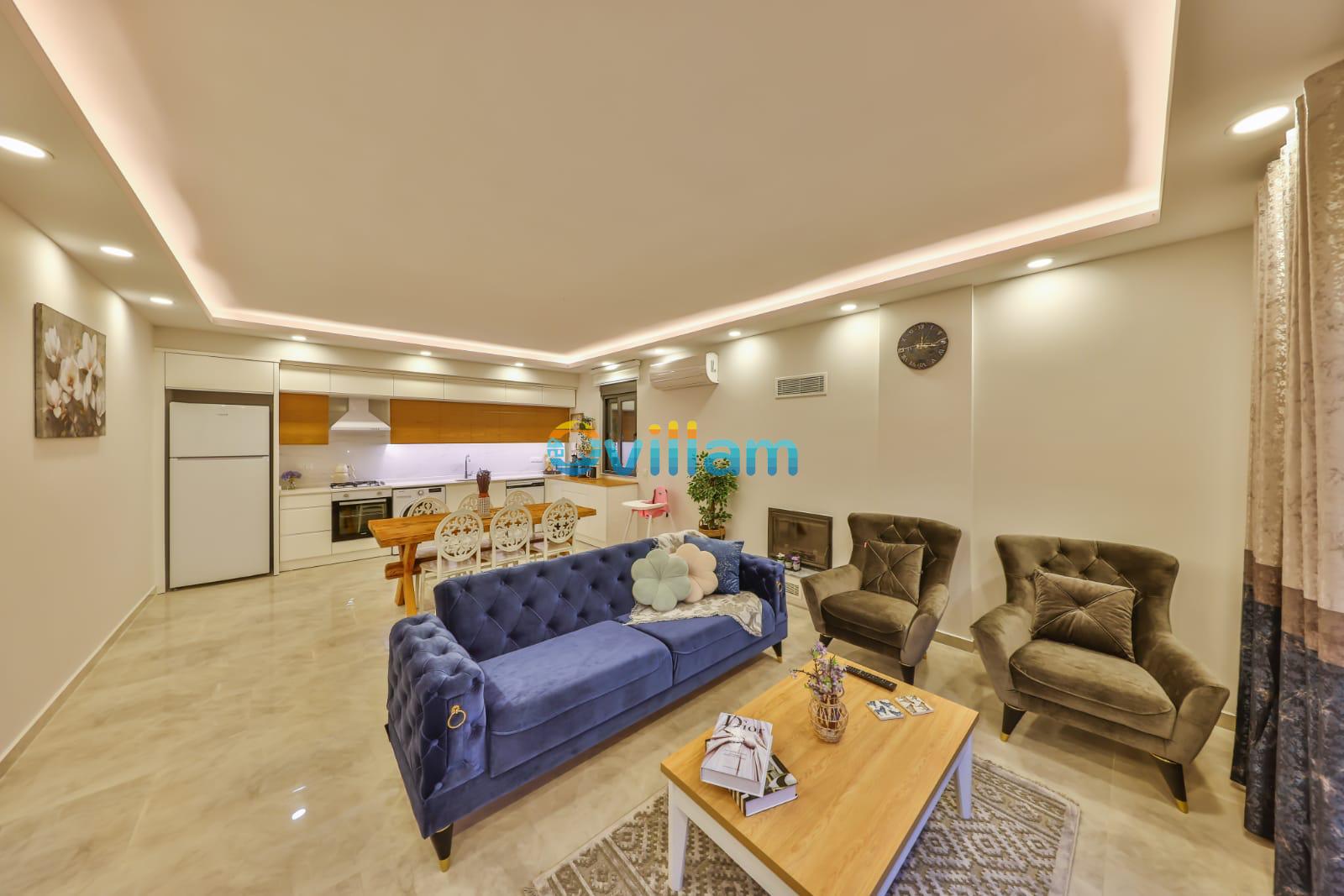 Mavi kadife kanepe, gri berajerler ve açık mutfaklı modern salon.