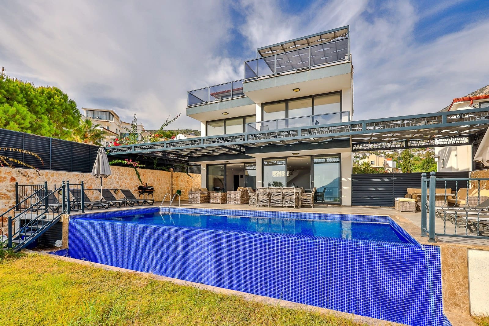 Önünde mavi havuz ve şezlonglar olan, iki katlı modern villa.