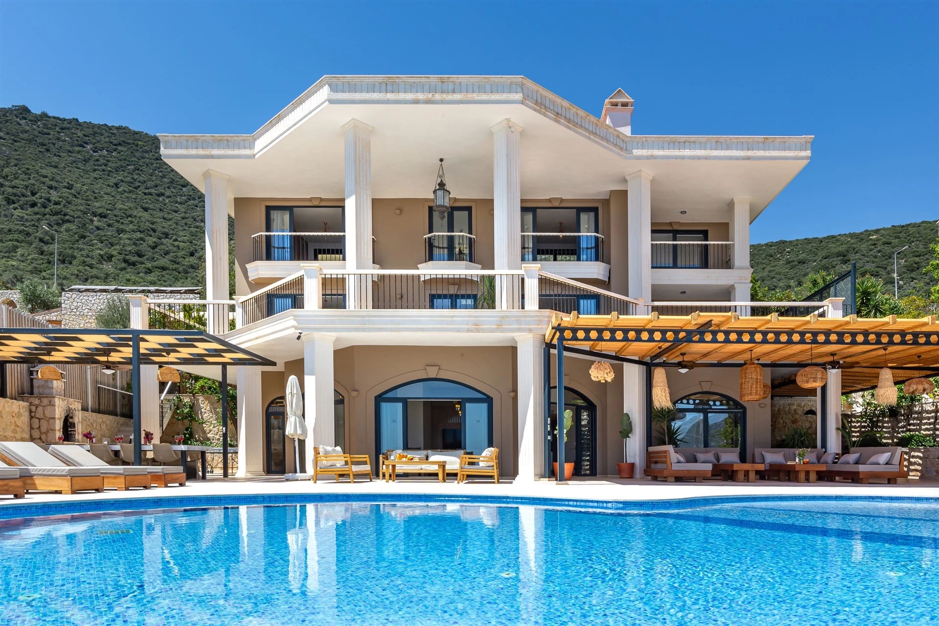 Önünde havuzu olan sütunlu lüks villa dış cephesi ve geniş terası.