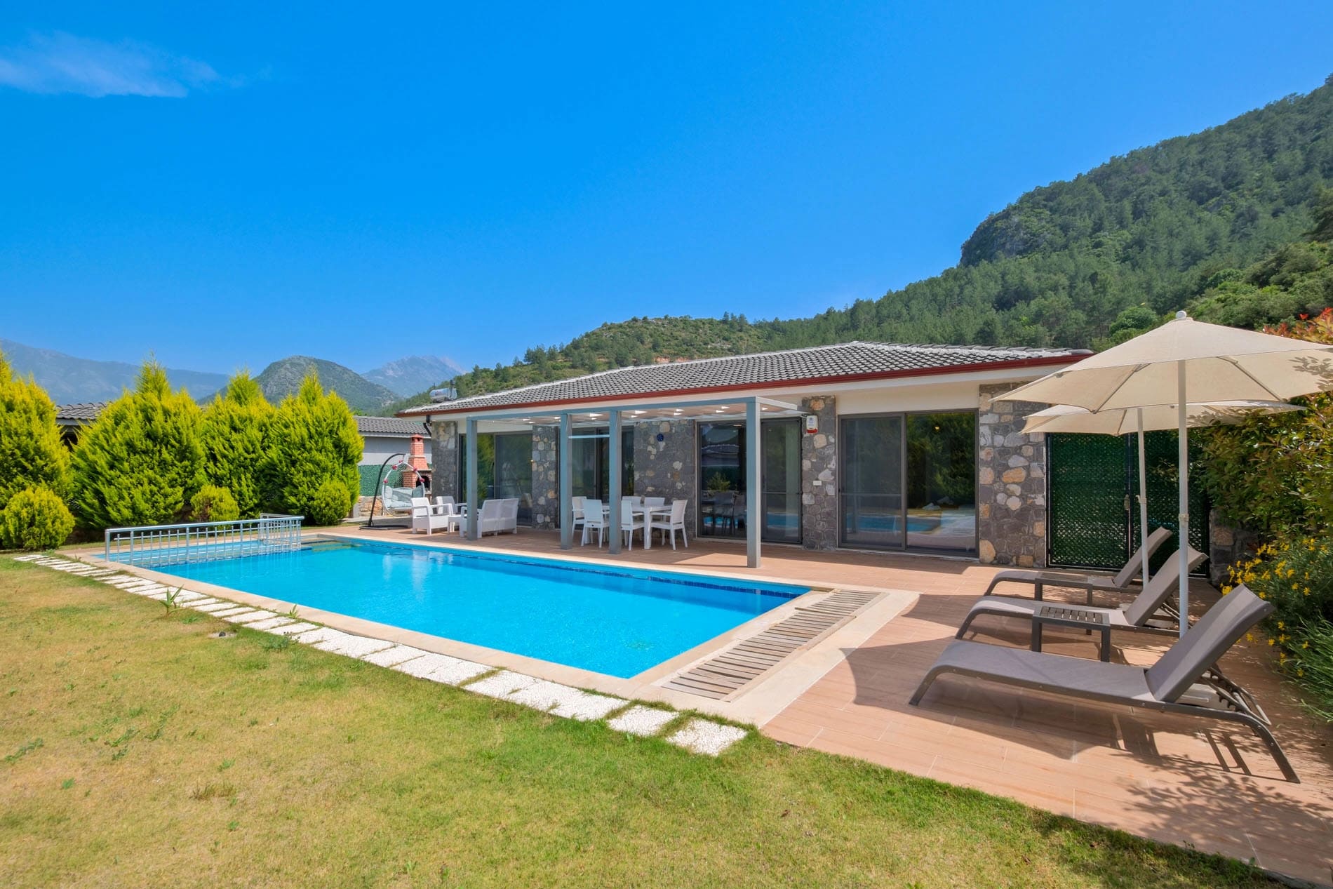Yüzme havuzlu ve şezlonglu villa dış cephe görünümü.