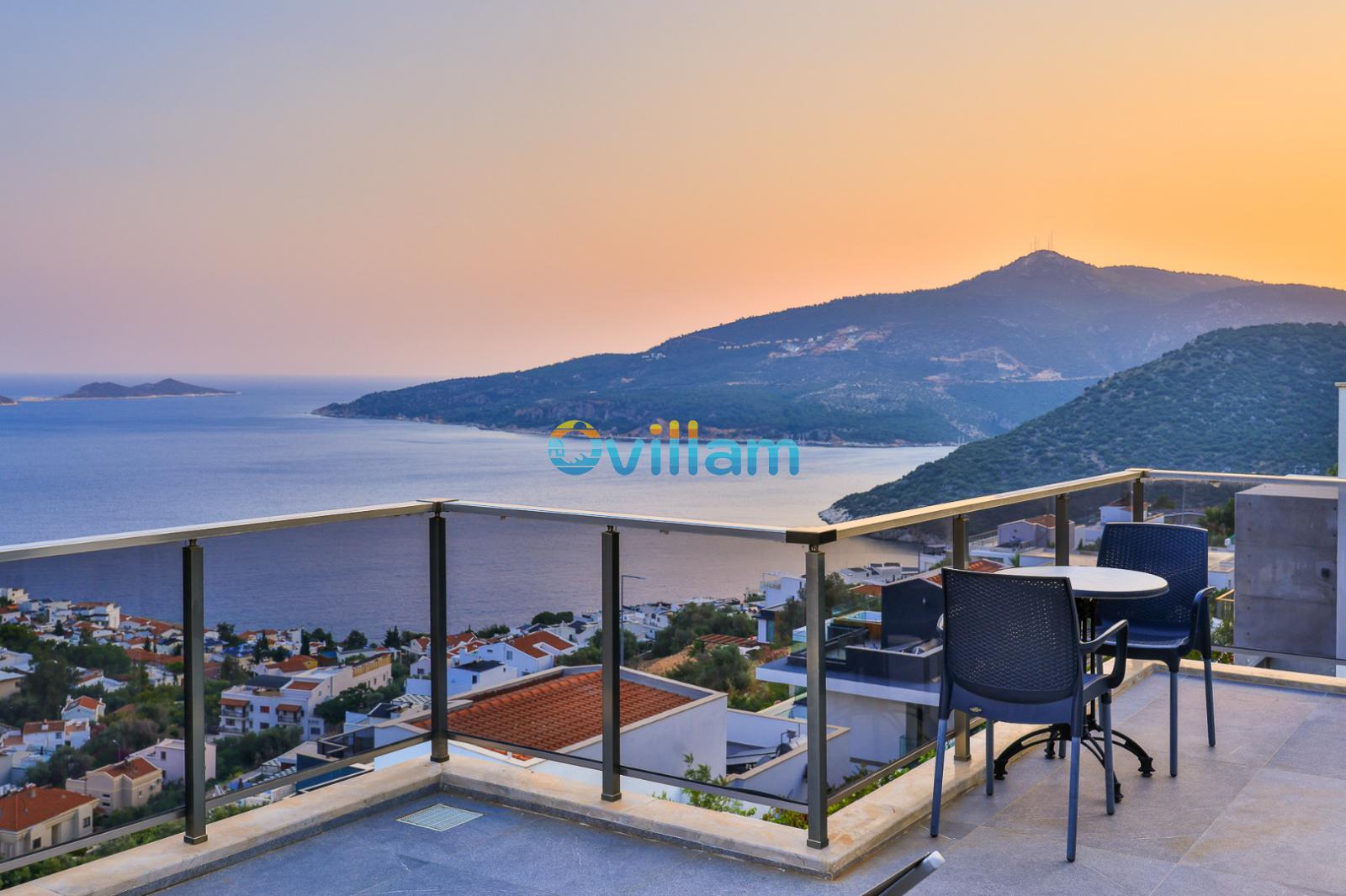 Balkonda masa ve sandalyeler ile ufukta deniz ve dağ manzarası.