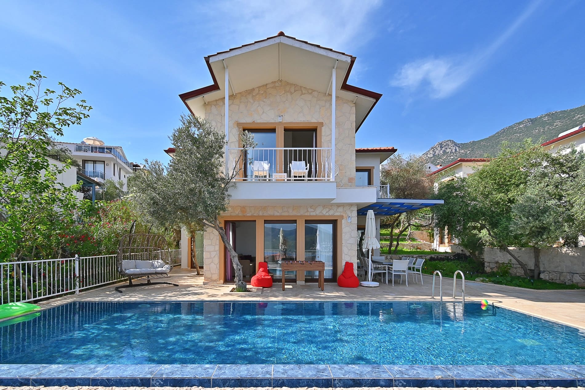 Taş cepheli, balkonlu iki katlı villanın önünde havuz ve bahçe alanı.