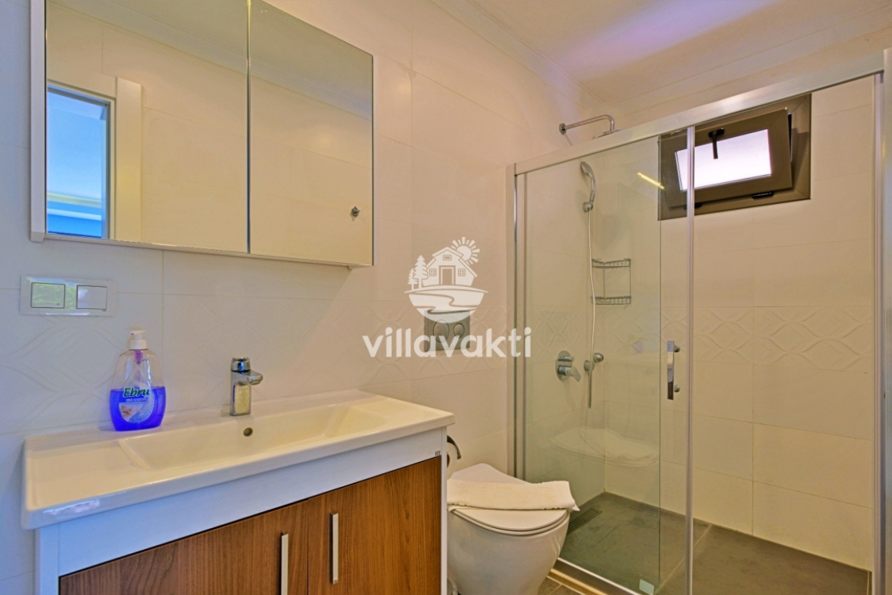 Beyaz lavabo dolabı, cam duş kabini ve klozet bulunan banyo.