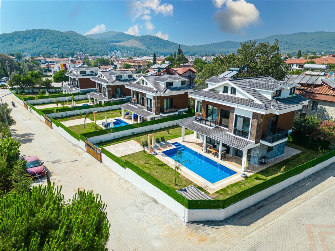 Önünde havuzu ve bahçesi olan, dağ manzaralı yan yana villalar.