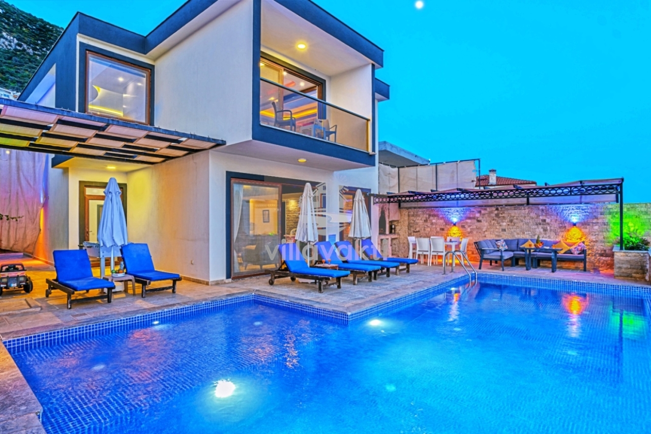 Aydınlatmalı havuzu ve şezlongları olan, taş duvarlı veranda ve modern villa.