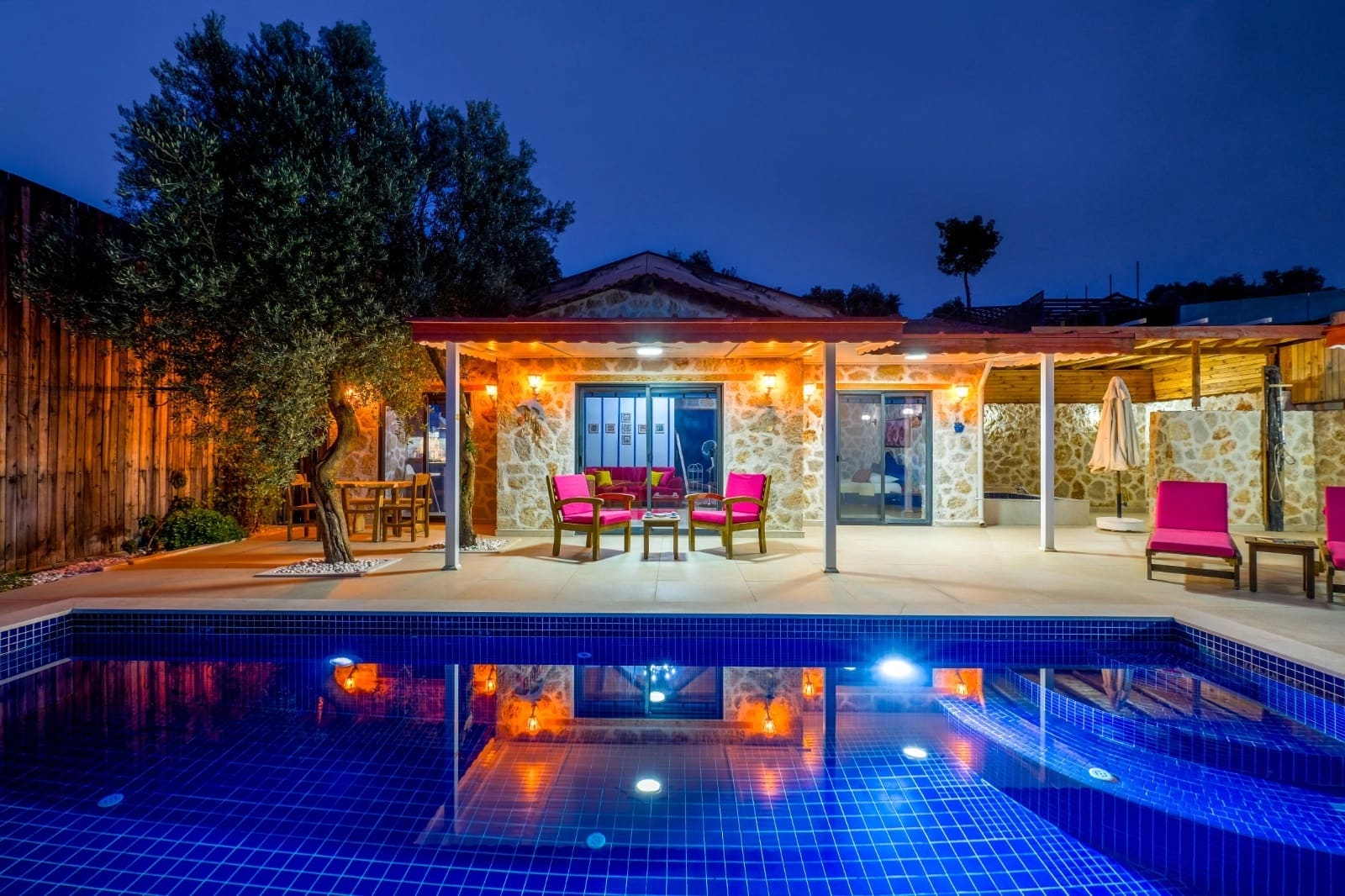Akşam ışıklandırmalı havuz başı ve taş villa verandası.