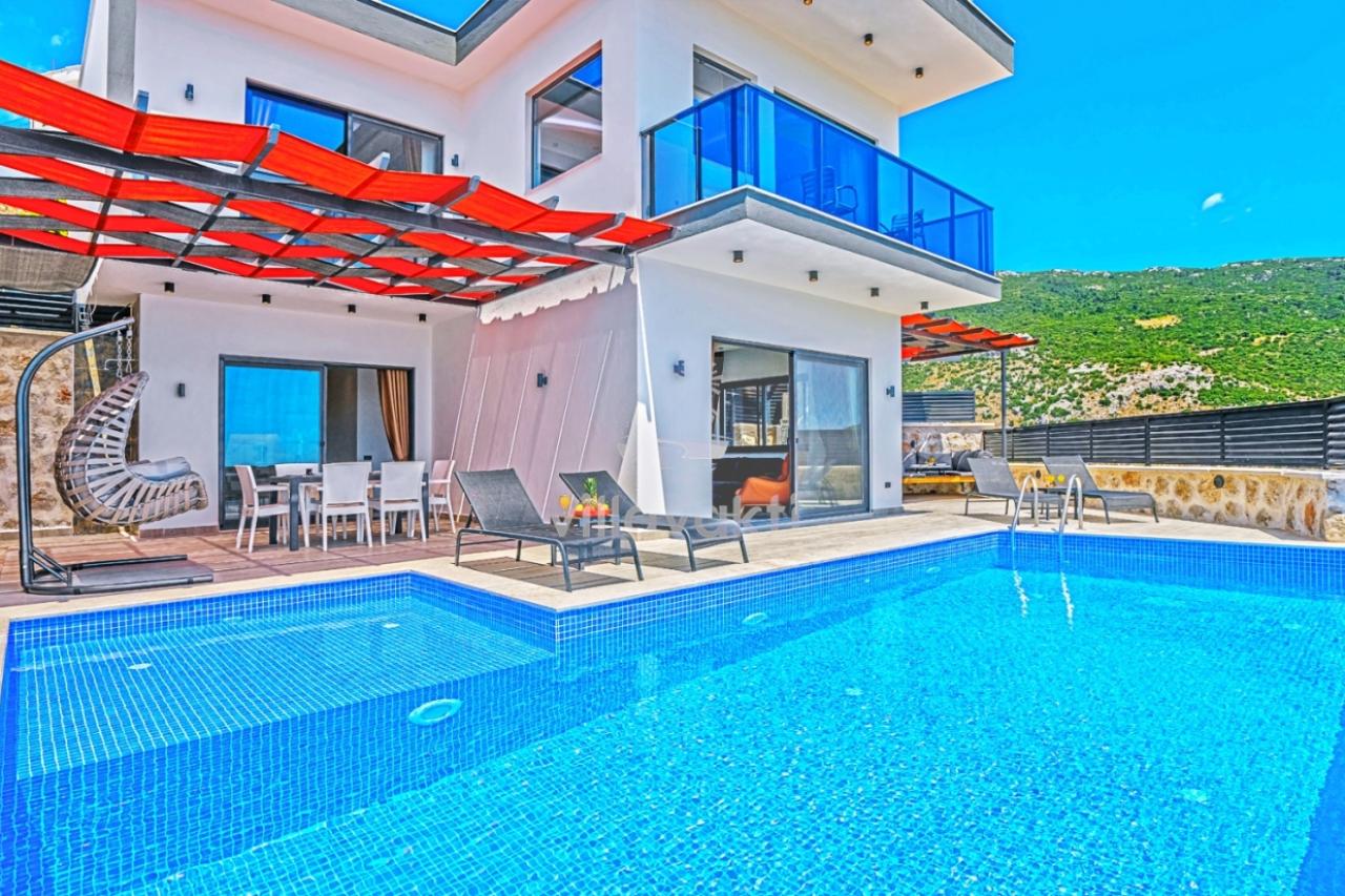 Havuz kenarında şezlonglar ve arka planda dağ manzaralı iki katlı villa