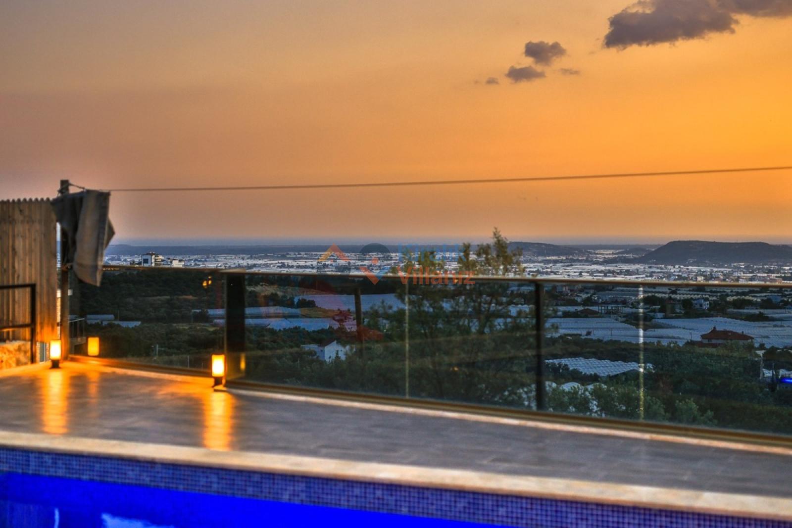 Akşamüstü cam korkuluklu balkondan görünen şehir ve ova manzarası.