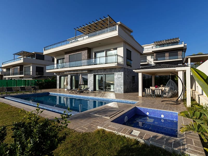 Mavi yüzme havuzu ve şezlongların bulunduğu modern villa dış cephesi.
