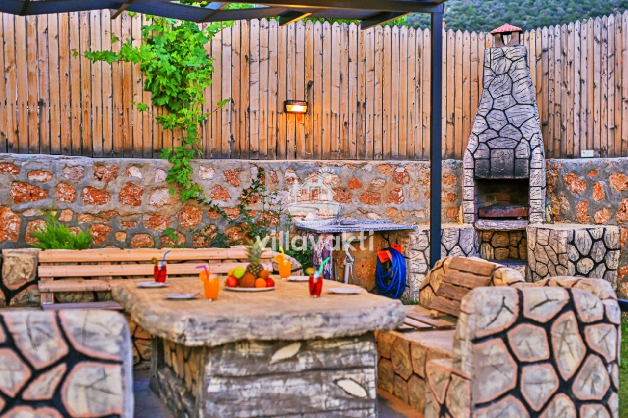 Bahçede taş masalı oturma alanı ve taş şömineli barbekü köşesi.