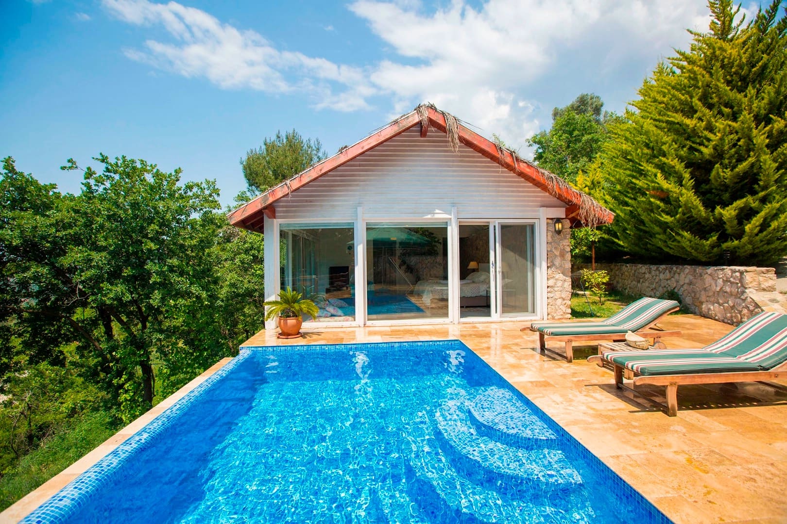 Beyaz ahşap cepheli, önünde havuz ve şezlonglar bulunan tek katlı villa.
