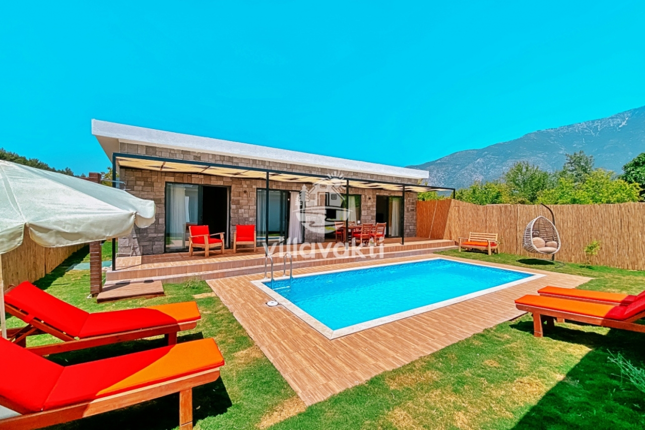 Havuz kenarında şezlonglar bulunan tek katlı taş villa ve dağ manzarası.