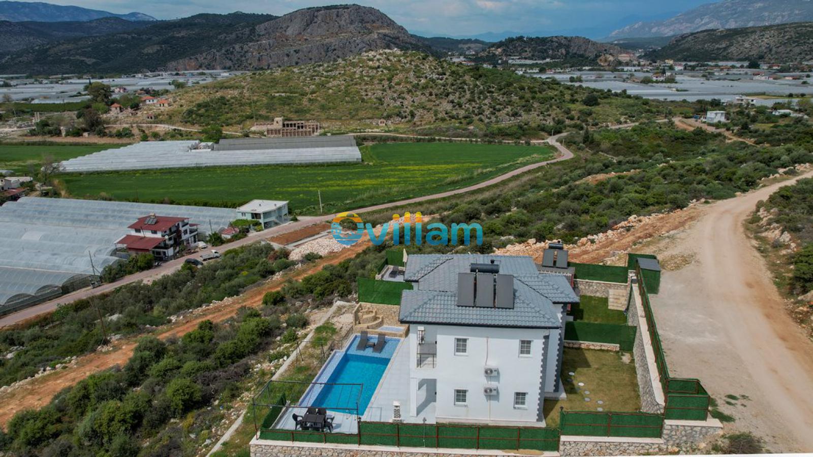 Dağ ve sera manzaralı yeşil doğa içinde konumlanan iki katlı beyaz villa.