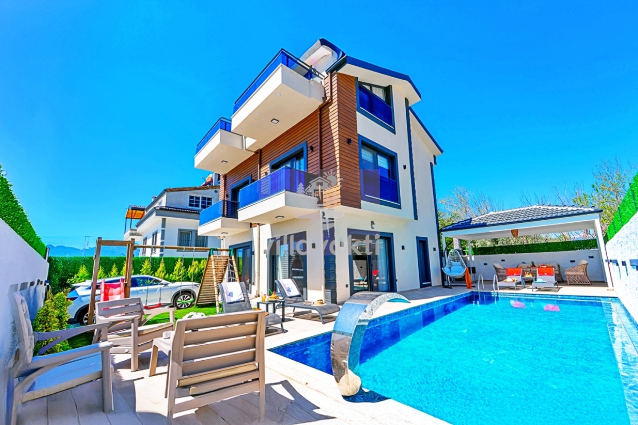 Mavi detaylı üç katlı modern villanın önünde özel yüzme havuzu ve şezlonglar bulunur.
