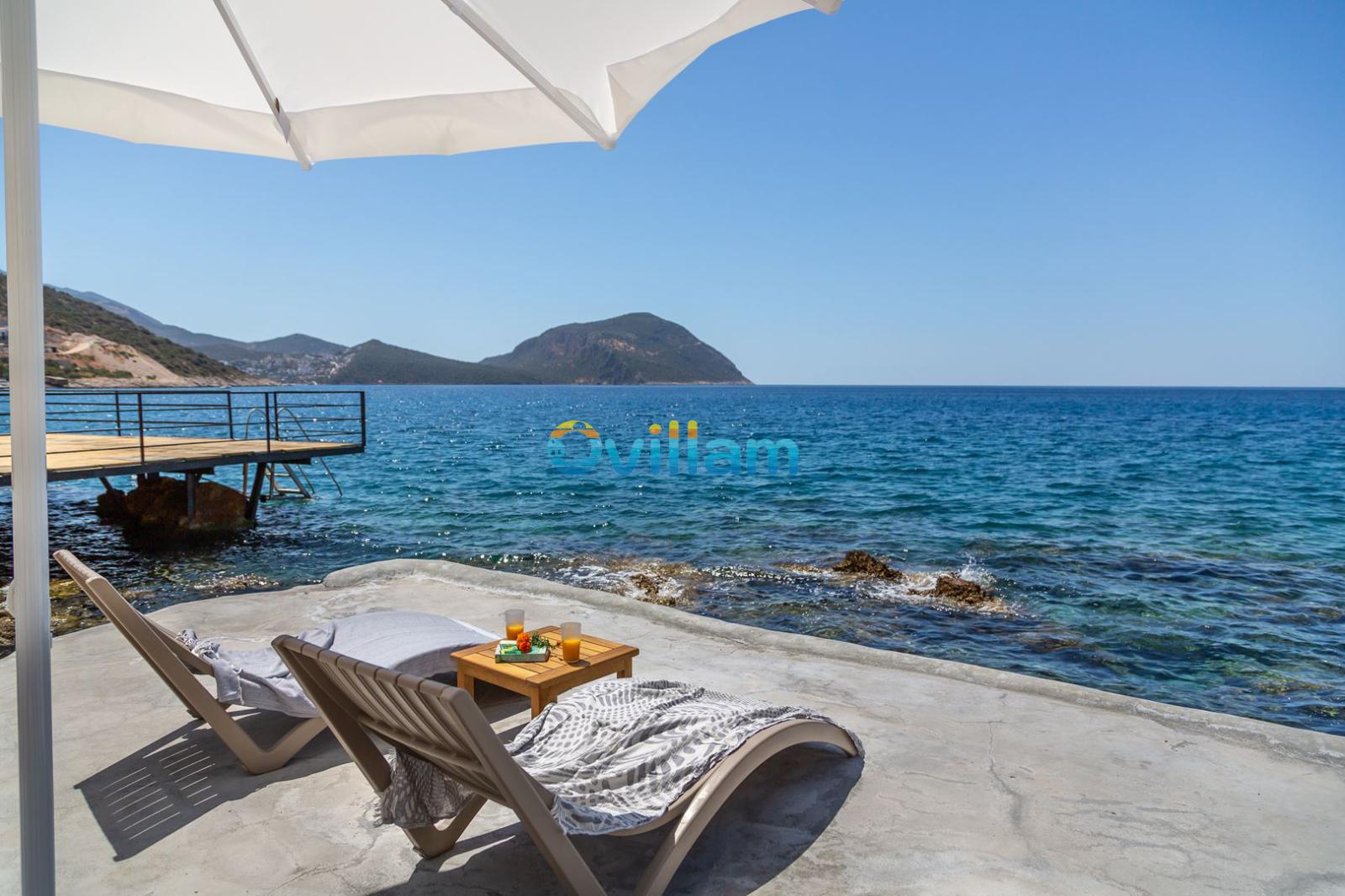 Deniz kenarında şezlonglar, şemsiye ve ahşap iskele manzarası.