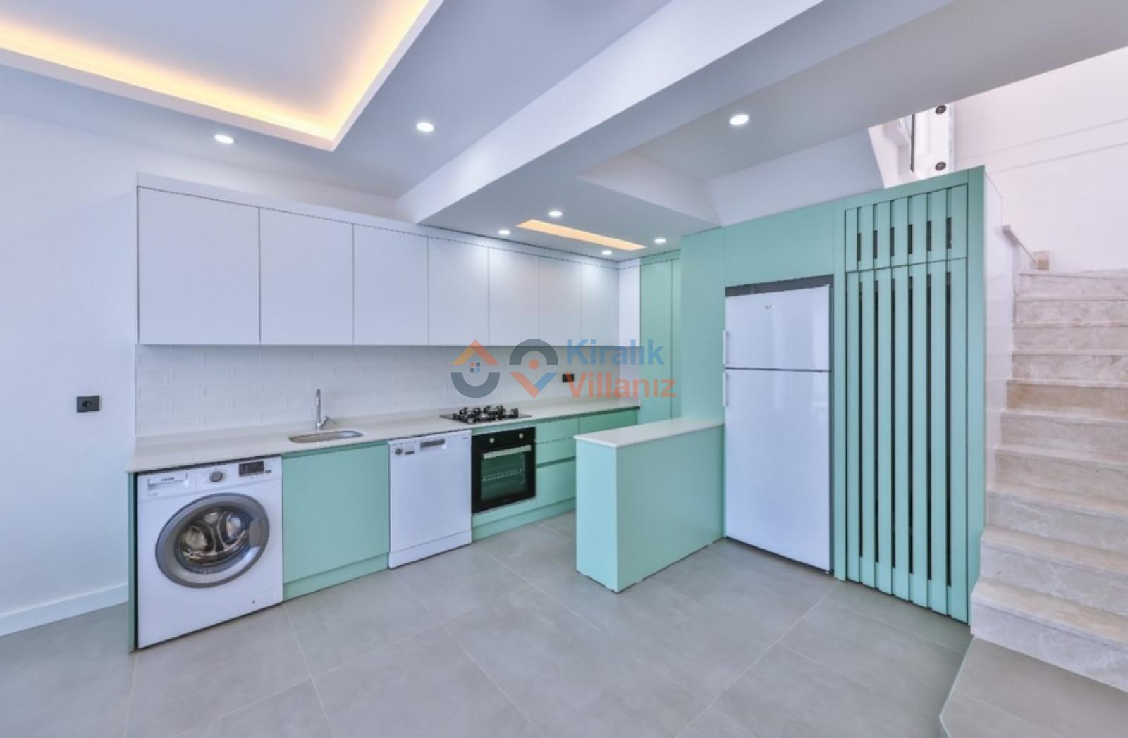 Mint yeşili dolaplı ve beyaz tezgahlı modern mutfak, çamaşır makinesi ve mermer merdivenler.