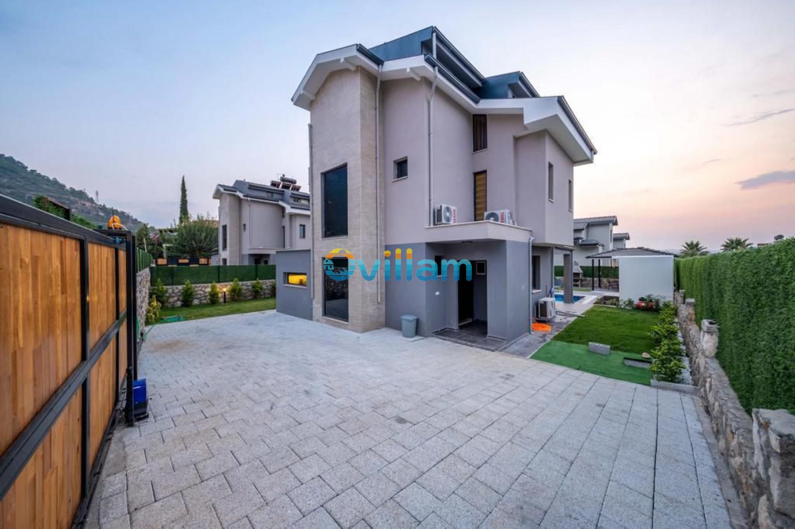 Geniş taş döşemeli park alanına sahip modern villanın dış cephesi.