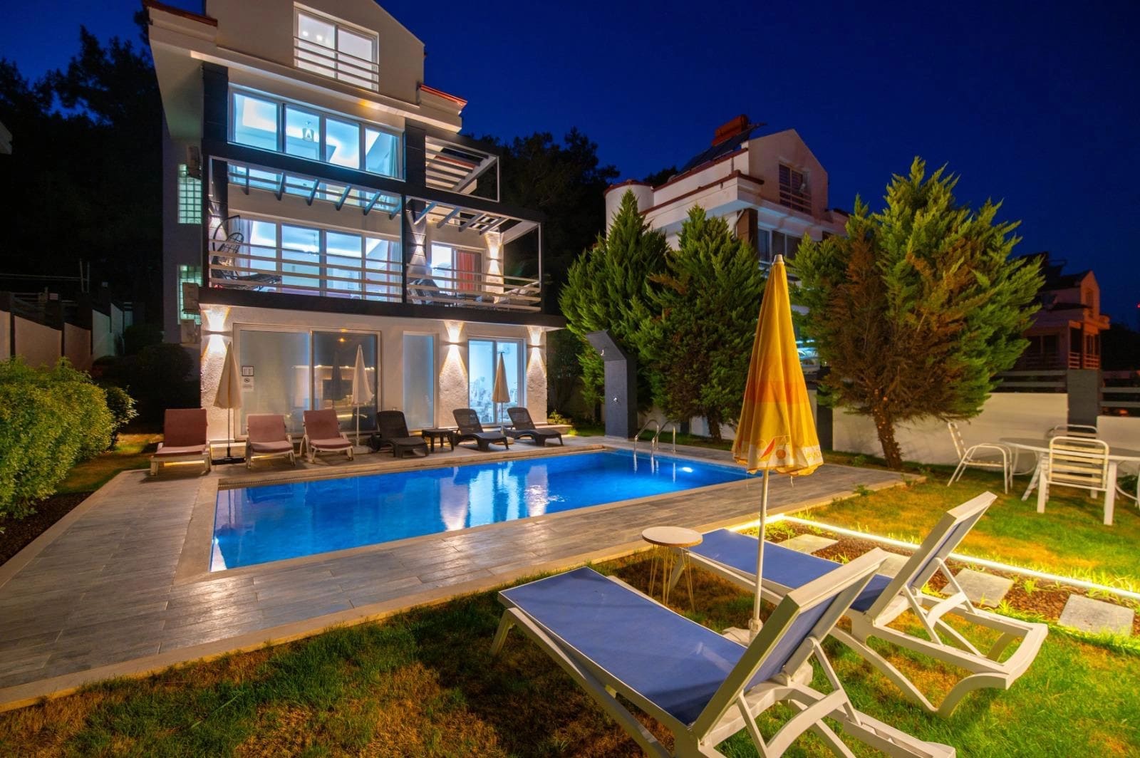 Gecesi ışıklandırılmış, havuzu ve balkon katları olan villa dış cephesi.