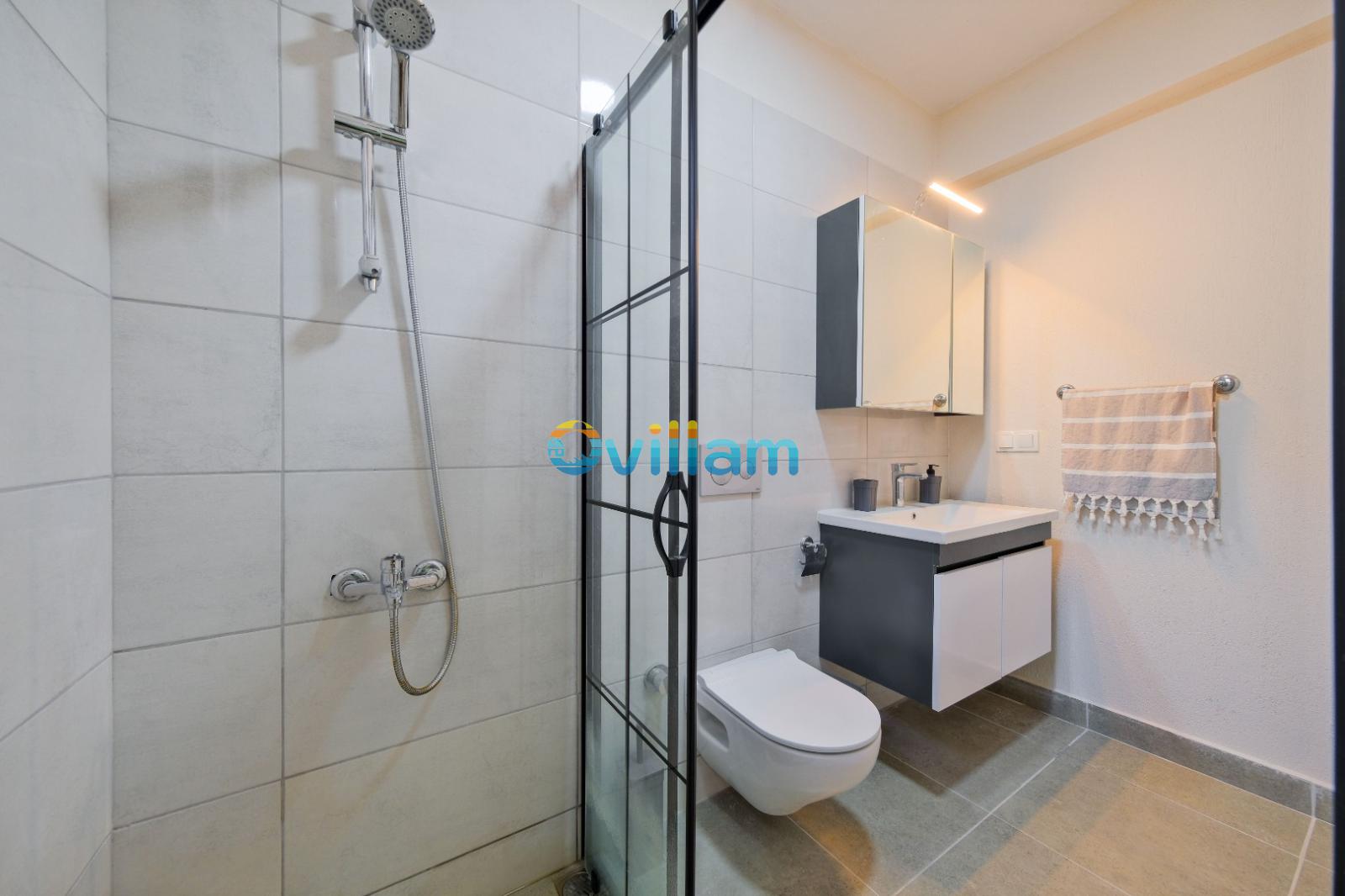 Cam bölmeli duş, asma klozet ve gri tonlarında lavabo dolabı içeren banyo.