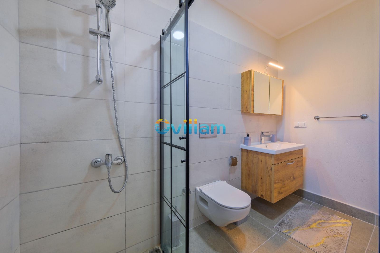 Cam kabinli duş, asma klozet ve ahşap dolaplı lavabo bulunan modern banyo.