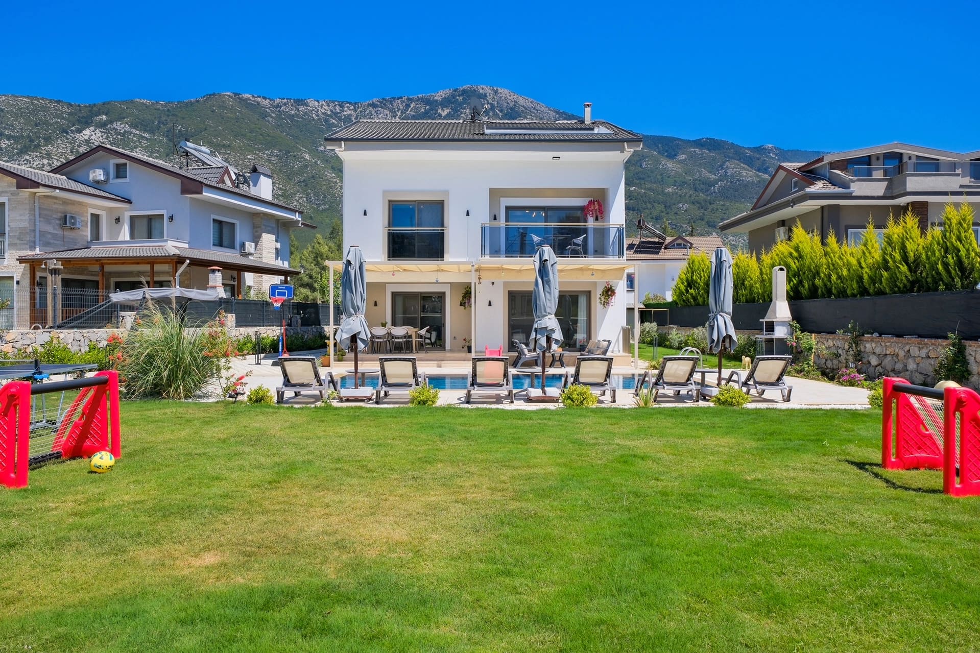 Bahçesinde havuz ve şezlonglar bulunan iki katlı beyaz villa.