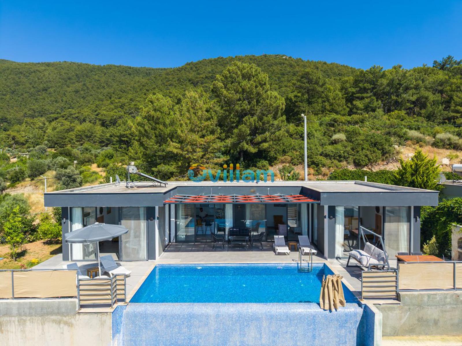 Orman manzaralı, önünde havuz ve şezlonglar bulunan tek katlı villa.