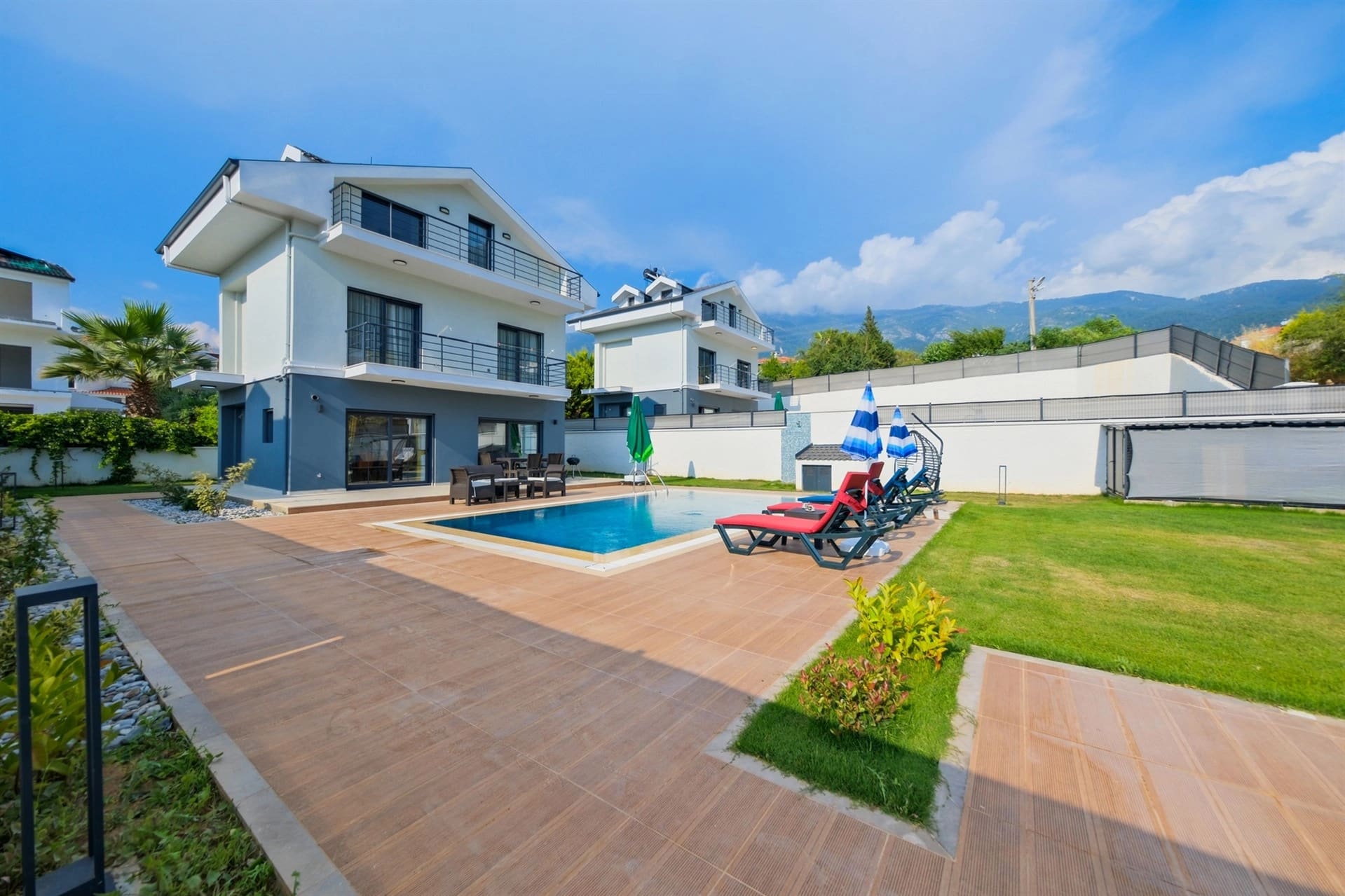 Dağ manzaralı arka bahçesinde havuz ve şezlonglar bulunan iki katlı villa.