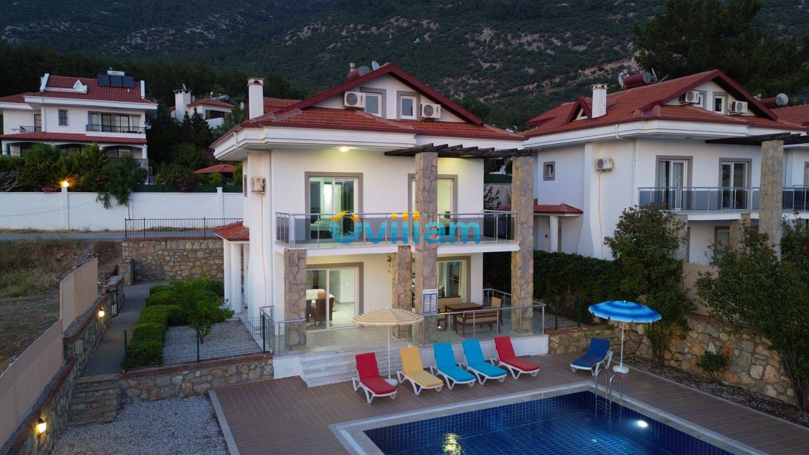Dağ manzaralı, önünde havuzu ve şezlongları bulunan iki katlı müstakil villa.