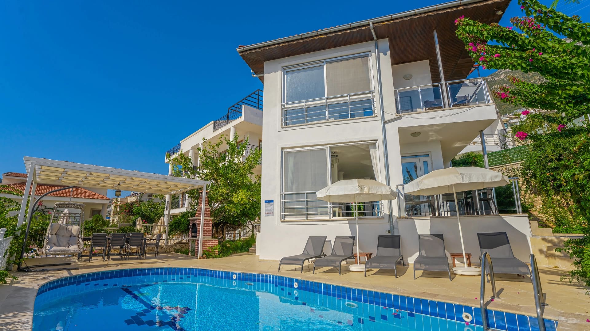 Önünde havuz, şezlonglar ve veranda bulunan beyaz dış cepheli villa.