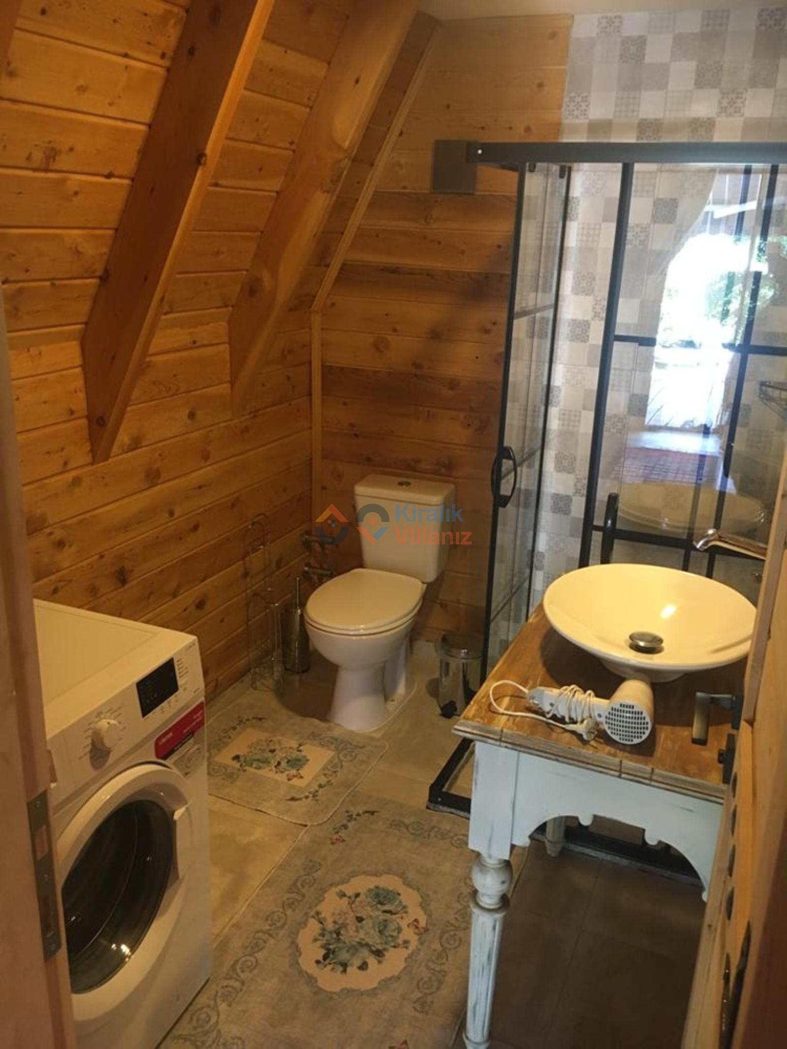 Ahşap duvarlı banyoda duşakabin, lavabo ve çamaşır makinesi.