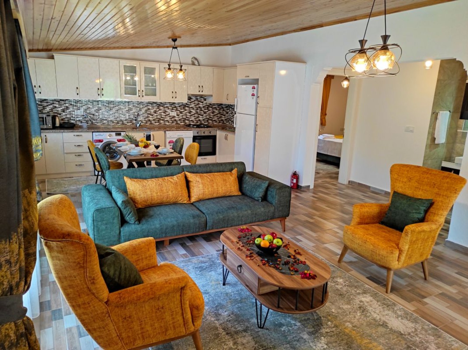 Ahşap tavanlı, açık mutfaklı, yeşil koltuklu ve sarı berjerli modern oturma odası.