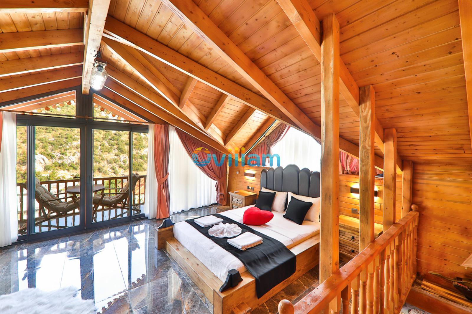 Ahşap tavanlı çatı katı yatak odasında çift kişilik yatak ve balkon kapısı.