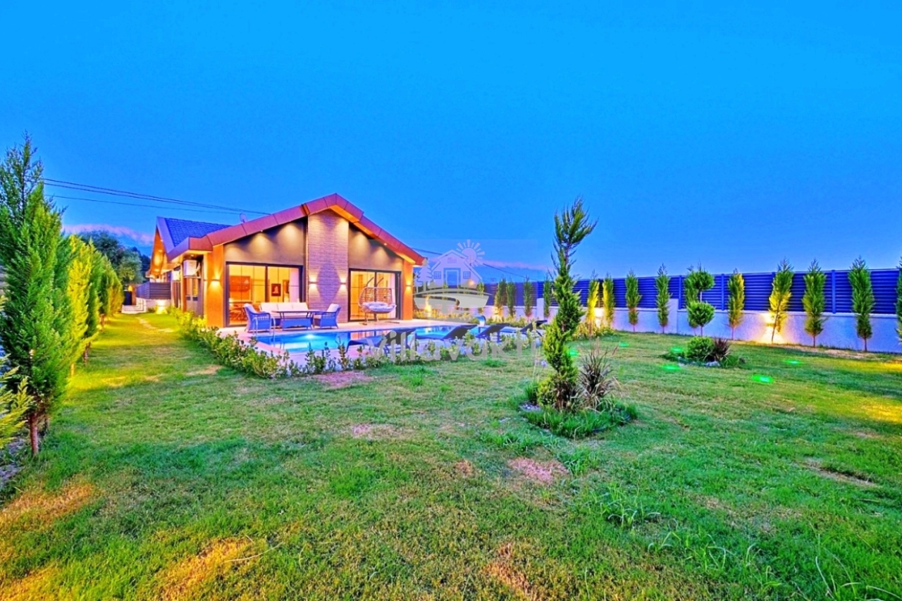 Bahçesinde havuz bulunan, akşam aydınlatmalı tek katlı villanın geniş çim alanı.