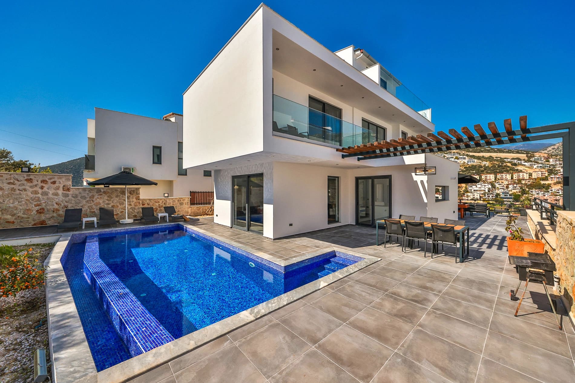 Bahçesinde özel havuz ve yemek masası yer alan beyaz dış cepheli modern villa.